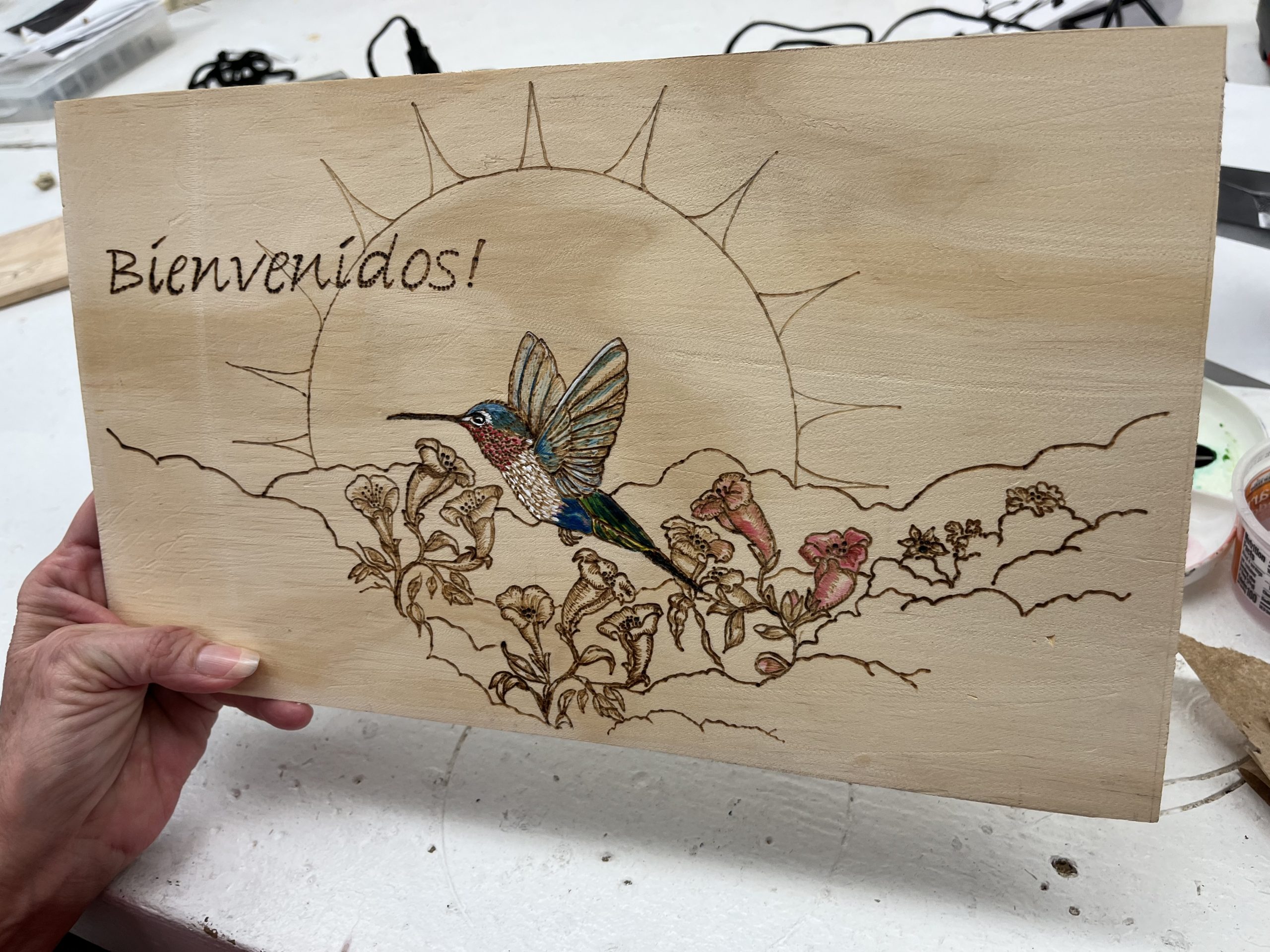 A beautiful wooden sign of a hummingbird flying over flowers created by one of the inmates in the Woodworking program