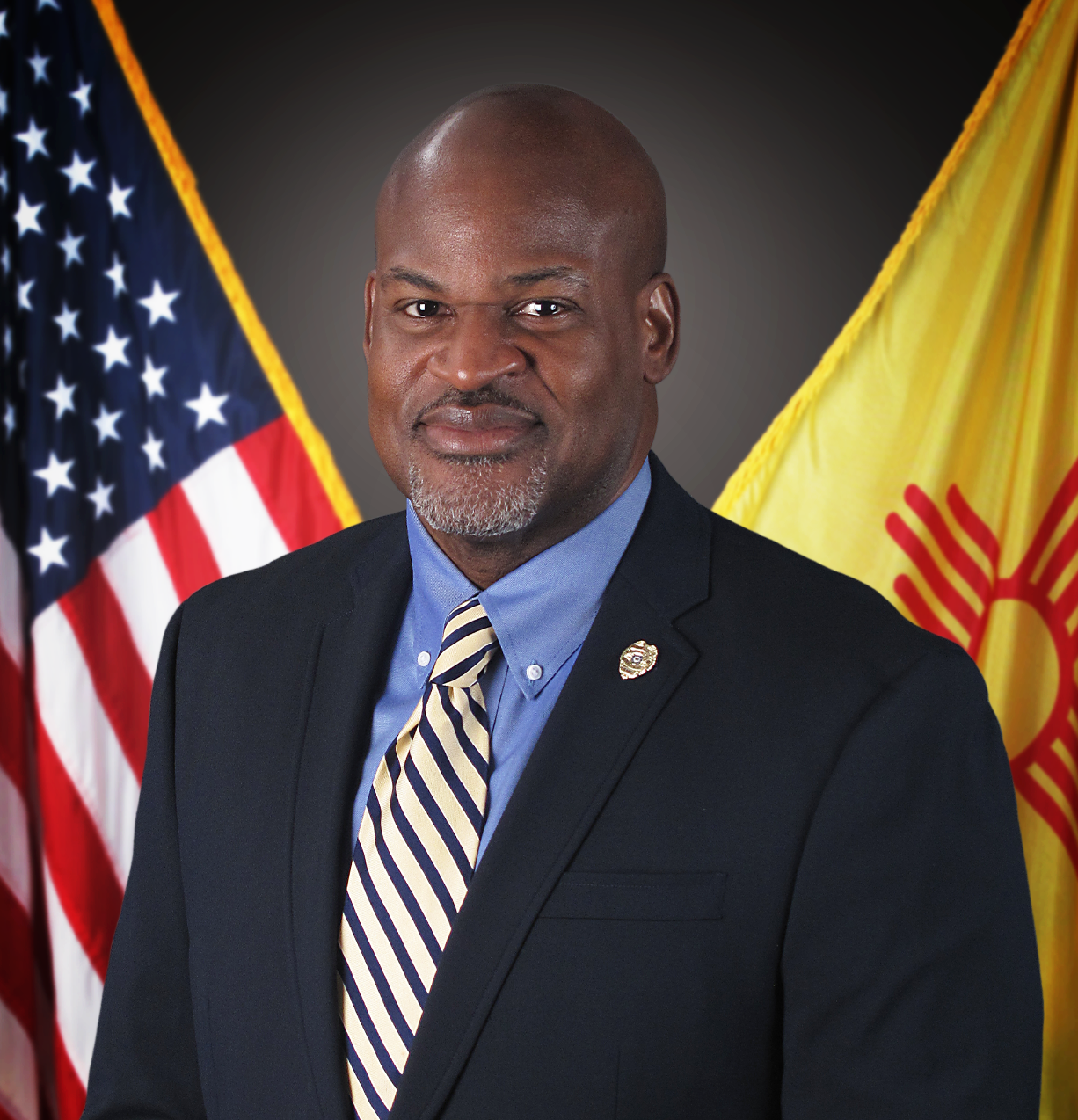 Headshot of Director Brown against United States flag and New Mexico flag background